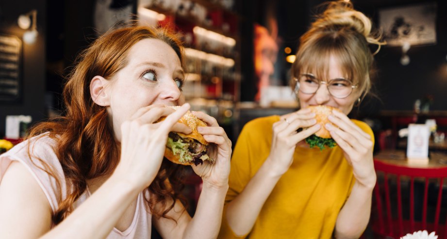 Two female friends eating burger in a restaurant, © Westend61